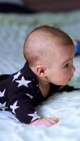 Little infant boy tries to hold his head as lies on bed. Adorable child looks in front of himself attentively. Side view. Vertical video