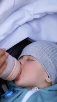 Sleepy adorable baby being fed from bottle during walk. Caucasian child lies in stroller falling asleep and suckling bottle. Close up. Vertical video