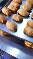 Freshly baked pastry on baking sheets are piled on shelves. Croissants and bagels production at bakery. Close up. Vertical video