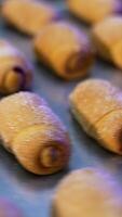 Savory delicious little croissants sprinkled with sugar at baking sheet. Tray full of desserts on a turning table. Close up. Vertical video