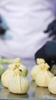 Bakers make tiny bags with stuffing from dough. Close up. Handmade sweet desserts manufacturing at confectionary factory. Vertical video