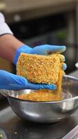Food factory worker covers the cakes with yellow sprinkling. Close up. Ready-made desserts being put in separate boxes. Blurred backdrop. Vertical video