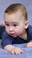 Beautiful adorable baby boy lies on soft plaid. Little kid looking at something with interest with open mouth. Close up. Grey backdrop in blur. Vertical video