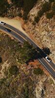 Mountainous landscape overgrown with moss and few trees. Highway in the rocky area with cars moving by. Aerial view. Vertical video