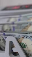 A wad of one hundred dollar bills being counted in cash machine. Apparatus for counting money blurred close up. Vertical video