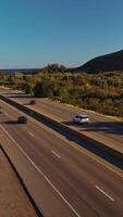 Two-ways roads going through the humpy mountainous territory. Transport moving by the highways at the backdrop of blue skies. Vertical video