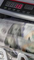 Automatic cash machine for bank operations. Modern device counting one hundred dollar bills. Close up. Vertical video