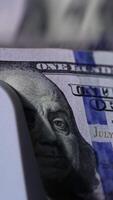 Benjamin Franklin portrait on the dollar bills. Cash counting machine counts American currency bills. Close up. Vertical video