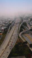 Big city panorama covered with thick fog at daytime. Multilane roads with cars going into hazy horizon of San Francisco. Top view. Vertical video
