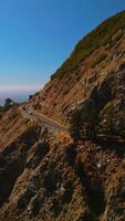 Freeway in the mountains with cars moving quickly. Beautiful rocks of Big Sur Morro Bay by the ocean at the backdrop of blue clear sky. Vertical video