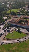 Green city scenery on summer day. Approaching beautiful Old Mission Santa Barbara with a lively traffic road. Top view. Vertical video