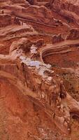 Beautiful canyons of red color with rounded tops and edges. Curved road going around the rocks. Top view. Vertical video