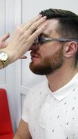 Checking eyesight. Doctor customises lenses on trial frame to a patient. Profile view of a young man in testing glasses in optical clinic. Vertical video