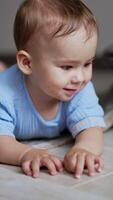 Nice cute child lies on the floor watching the ball rolling in front of him. Little boy crawling up to the toy watching it move. Close up. Vertical video