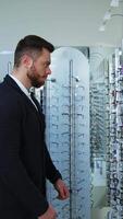 Male customer at eyewear store. Profile view of a handsome man choosing eyeglasses in the shop. Buyer in the optics. Vertical video
