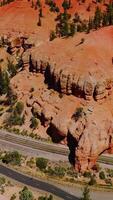 Sunlit panorama of amazing canyon rocks with pine trees growing on. Car roads in the mountains of Arches National park from aerial view. Vertical video