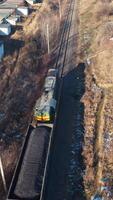 Cargo train on a railroad in sunny winter day. Top view on a freight train on the background of many garages from both sides. Aerial view. Vertical video