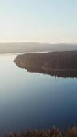 Beautiful view of nature. Wide river with blue calm water in the evening. Small island surrounded by water. Aerial view. Vertical video