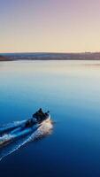 Two fishermen in motor boat in the evening. Speedboat moving on the water surface at sunset. Aerial view. Vertical video