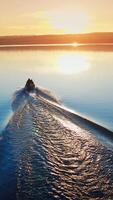 Motor boat floating on the river at sunset. Path on water after motion of motor boat on the background of a setting sun. Vertical video