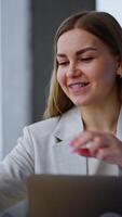Cheerful lady sits with laptop in front of her. Woman is interested in something aside and puts on the glasses to see it better. Vertical video