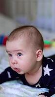 Curious interested little guy struggles to keep his head up to look around. Adorable baby boy lie on his belly on white backdrop. Vertical video