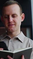 Mature man holds the notebook opened in front of him and print something on the phone. He throws interested look into the window. Vertical video