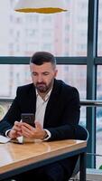 Bearded man looks at the screen of his smartphone. Businessman looks concerned searching for information, using gadget. Vertical video
