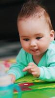 Beautiful baby boy lying on the colorful mat clapping hands by the floor. Funny kid stuck out his tongue and looks at the bottle in front of him. Vertical video