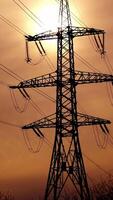 Transmission lines against the evening sky. High-voltage electric towers with wires on the setting sun background. Black pylons with electricity. Vertical video