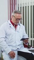 Confident family therapist working online. Doctor in white gown consulting people via internet using mobile phone in the office. Vertical video