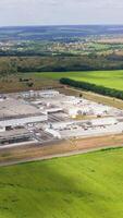 Modern industrial plant on field. Large factory among beautiful green nature. Agricultural center in the countryside. Aerial view. Vertical video