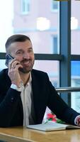 Successful businessman answering the phone in his office. Business talk in spacious light office. Business communication via smartphone. Vertical video