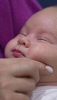 Sleepy newborn kid doesn't want to wake up lying in mum's hands. Mother is touching her baby's plump cheeks trying to wake him up. Close up. Vertical video