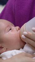 Newborn baby boy having meal and slowly falling asleep. Tiny boy in mother's hands going to sleep while feeding. Adorable kid close up. Vertical video