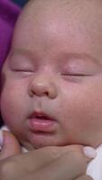 Face of an infant baby sleeping deeply and doesn't want to wake up. Loving mum trying to wake her kid up and touches his sweet cheeks tenderly. Close up. Vertical video