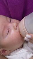 Beautiful newborn boy resting in mother's hands and being fed from a bottle. Little child closing eyes and gradually falling asleep. Close up. Vertical video