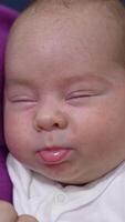 Baby doesn't want to wake up and barely opens his eyes. Mother is touching baby's nose gently to wake him up. Close up. Vertical video