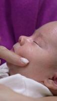 Beautiful infant in mother's embraces sleeps sweetly. Mother is trying to wake her son up by touching his chin, nose, cheeks. Cute boy doesn't want to wake up. Vertical video