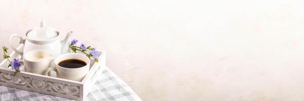 Chicory tea, teapot, milk jug on white wooden tray on plaid napkin. Banner. Copy space. photo