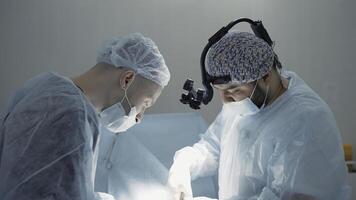 Two surgeons busy at work . Action . Two men in blue lab coats are painstakingly working on a complex operation , using various medical accessories like microscopic glasses photo