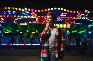 A cute Caucasian boy, a child, came to the amusement park to have fun, play and ride a merry-go-round. A child standing in front of a merry go round photo
