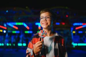 A cute Caucasian boy, a child, came to the amusement park to have fun, play and ride a merry-go-round. A child standing in front of a merry go round photo