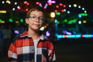 A cute Caucasian boy, a child, came to the amusement park to have fun, play and ride a merry-go-round. A child standing in front of a merry go round photo
