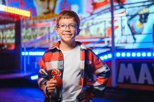 A cute Caucasian boy, a child, came to the amusement park to have fun, play and ride a merry-go-round. A child standing in front of a merry go round photo