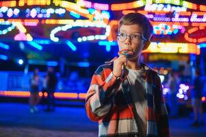 A cute Caucasian boy, a child, came to the amusement park to have fun, play and ride a merry-go-round. A child standing in front of a merry go round photo
