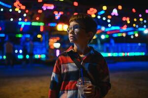 A cute Caucasian boy, a child, came to the amusement park to have fun, play and ride a merry-go-round. A child standing in front of a merry go round photo