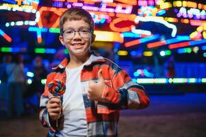 A cute Caucasian boy, a child, came to the amusement park to have fun, play and ride a merry-go-round. A child standing in front of a merry go round photo