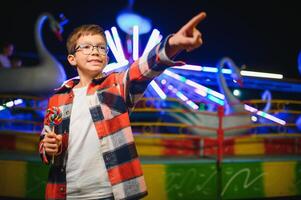 A cute Caucasian boy, a child, came to the amusement park to have fun, play and ride a merry-go-round. A child standing in front of a merry go round photo