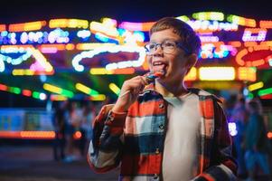 A cute Caucasian boy, a child, came to the amusement park to have fun, play and ride a merry-go-round. A child standing in front of a merry go round photo